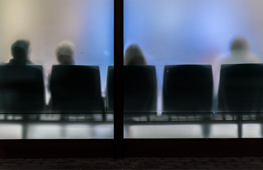 An abstract photograph of a waiting room with frosted glass and people sitting in chairs