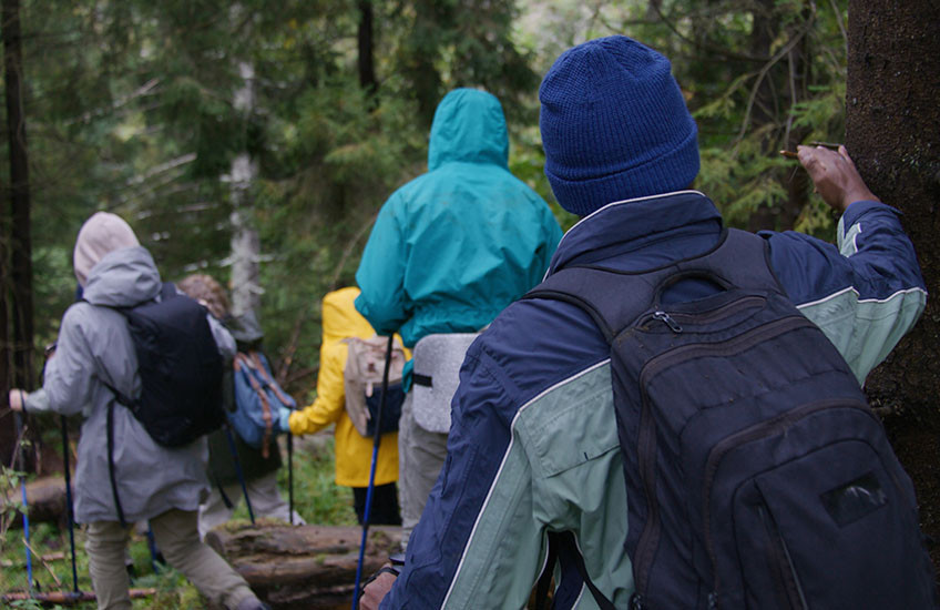 A group of young people hiking in the woods wearing jackets and hats.
