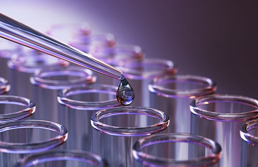 A drop of colorful fluid flows from a pipette into one of many vials in an array.