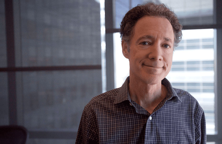 Portrait photo of Bruce Yankner in an office with window shades partially lowered