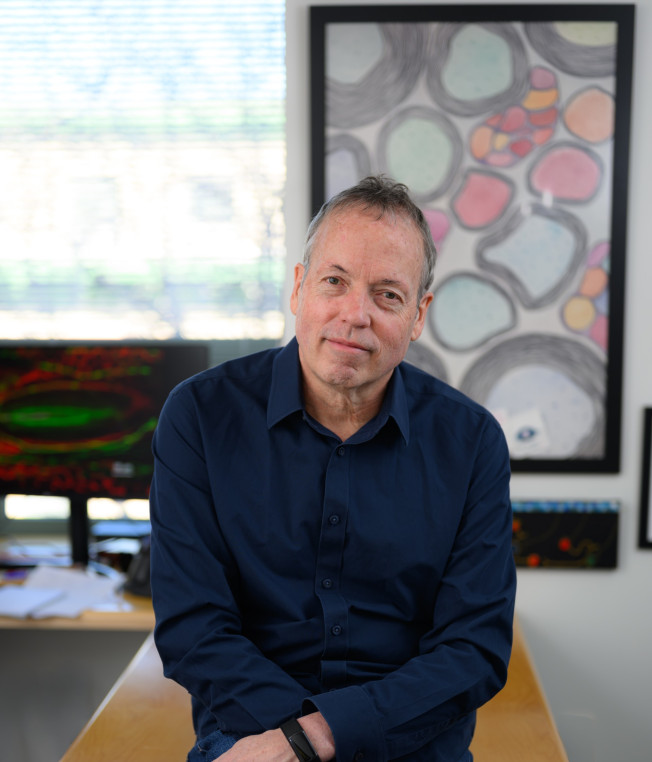 A man in a navy-blue shirt sitting on a table with his arms crossed