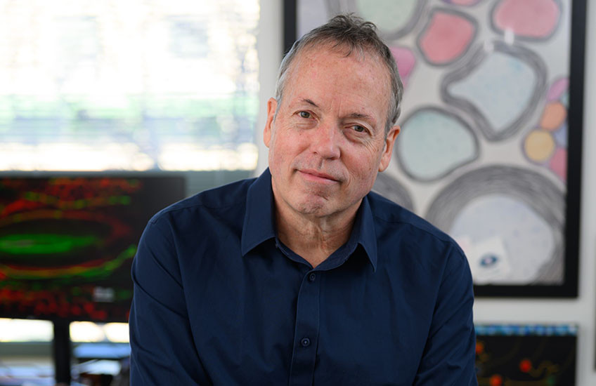 A man in a navy-blue shirt sitting on a table with his arms crossed