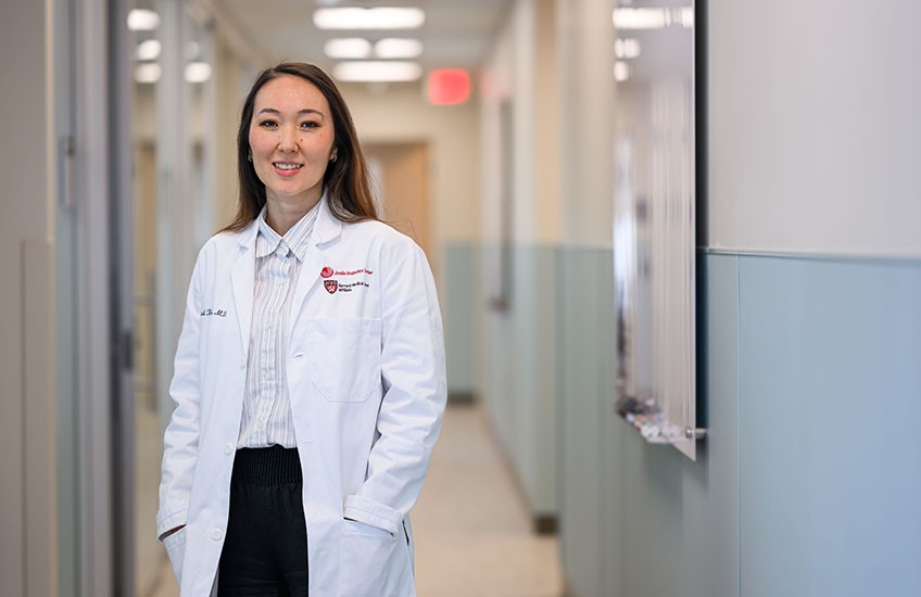 A woman in an HMS/Joslin white coat stands in a hallway.