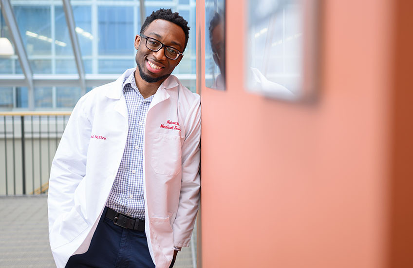 Leonard Nettey leans on a wall. He is wearing a white coat.