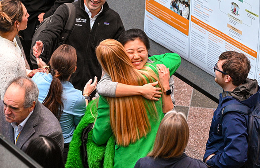 Two women hug in front of a research poster with six others nearby