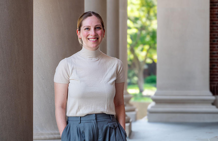 A smiling woman in a short-sleeve top stands outside with marble columns in the background.