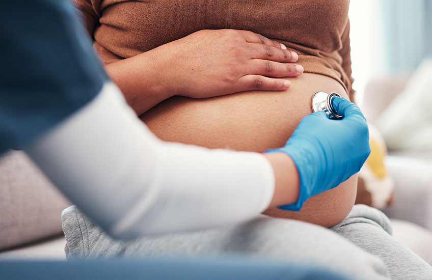 A doctor holds a stethoscope against a pregnant person’s belly