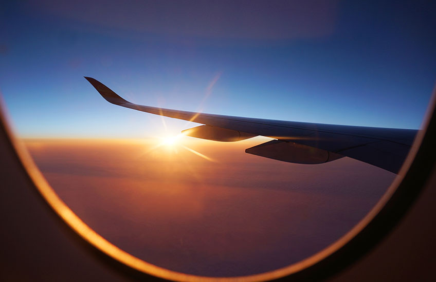 View out an airplane window of a plane’s wing at sunset.
