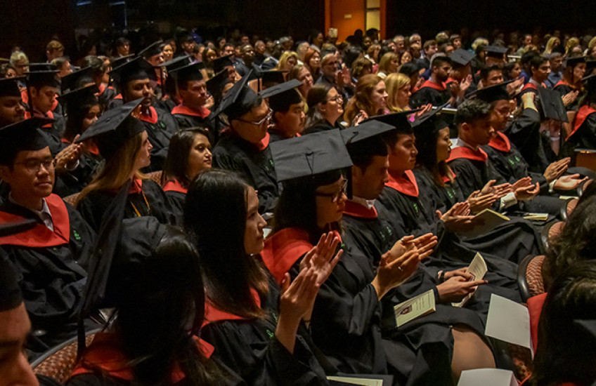 Audience shot of graduates in black and red regalia