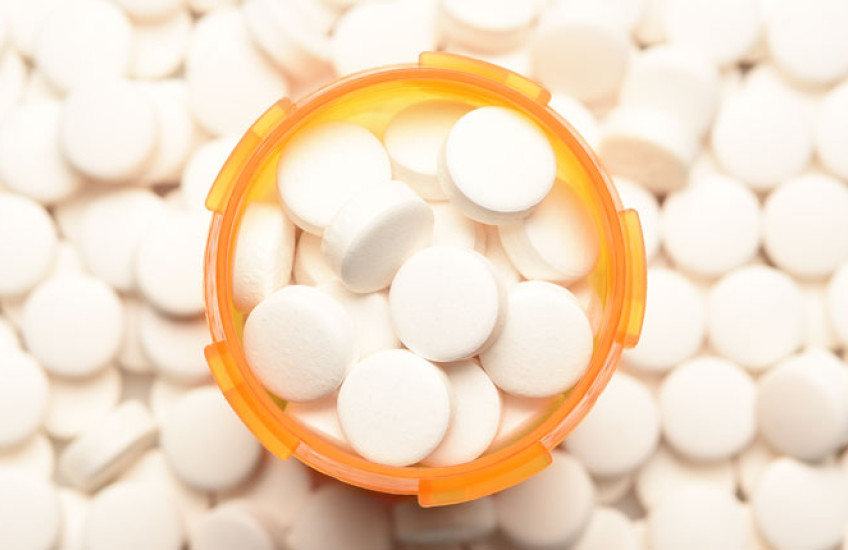 An aerial shot of an orange pill bottle filled with white round pills, surrounded by more of the same pills