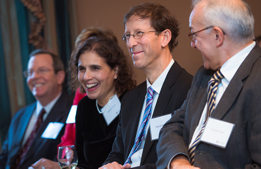 Four people sit smiling in a row with name tags