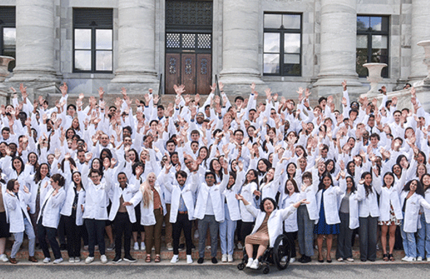 Entering students in white coats on steps of Gordon Hall raising arms and shouting with joy
