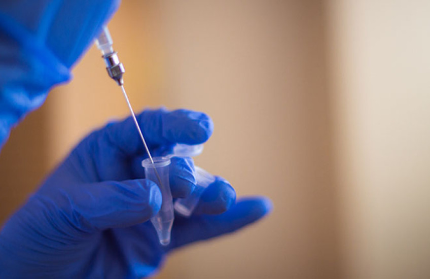 A gloved hand holding small vial and a second gloved hand holding a syringe