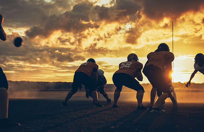 Photo of athletes playing football on a field at sunset