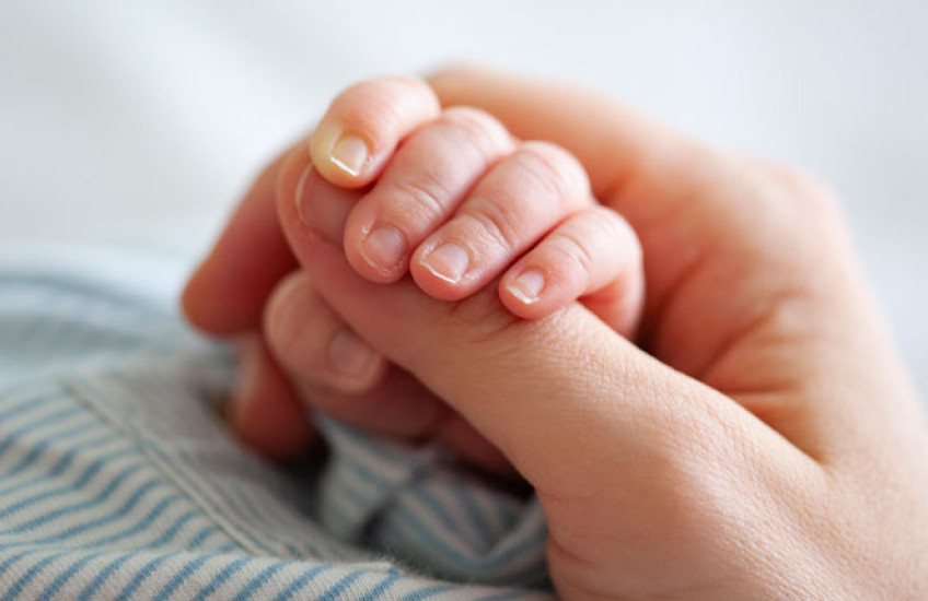 A close up of an adult grasping the hand of an infant 