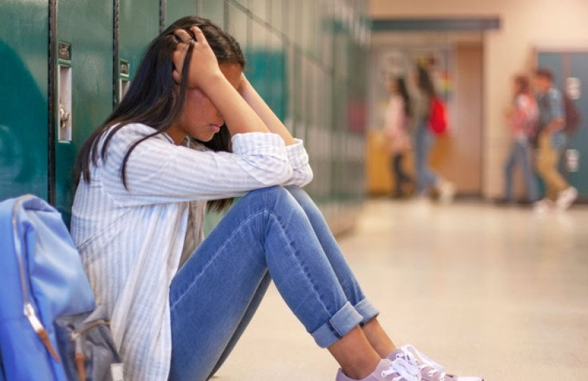 Image of a female high school student sitting on the floor by her locker, head in hands