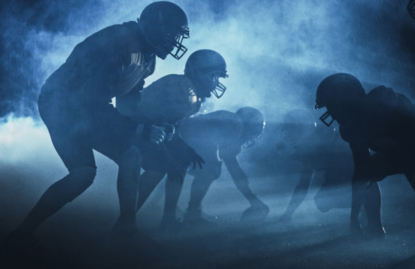 Backlight photo of football players in silhouette on playing field
