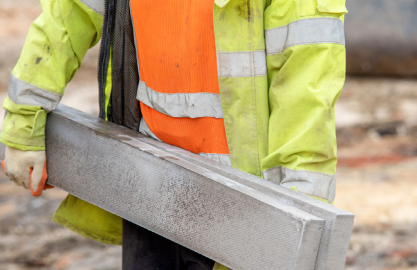 Photo of a construction worker carrying a large concrete beam 