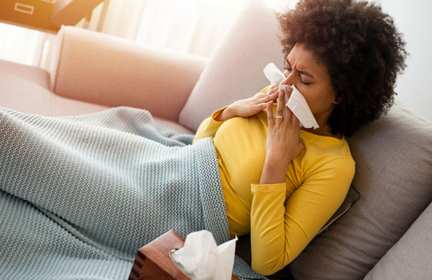 A sick person blowing their nose on a couch