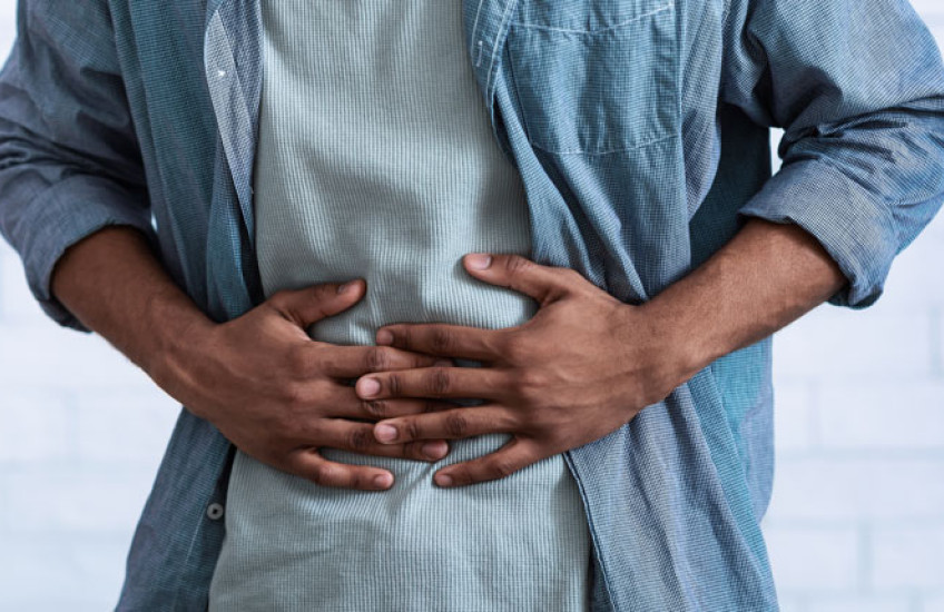 The torso of a person in a blue shirt with their hands over their stomach