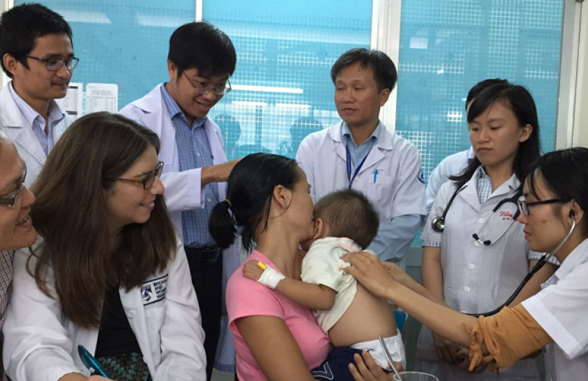 Photo of a group of medical students in Vietnam looking on as a baby is being examined in clinic. 