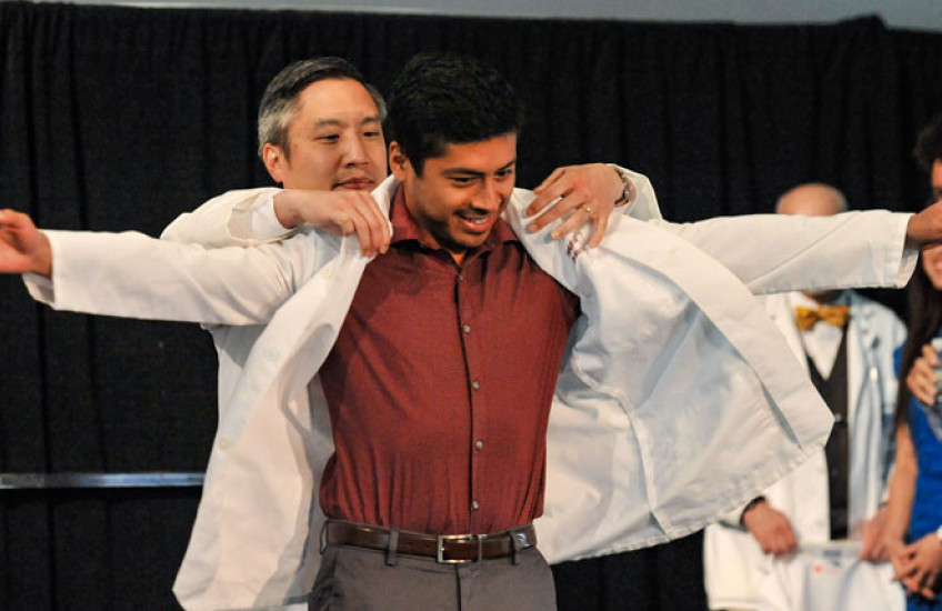 Chang, left, helps a student don his jacket during white coat ceremonies in 2021.  Image: Steve Lipofsky