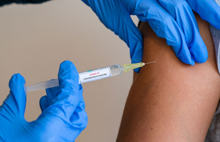 Image of gloved hands administering a vaccine shot to an arm 