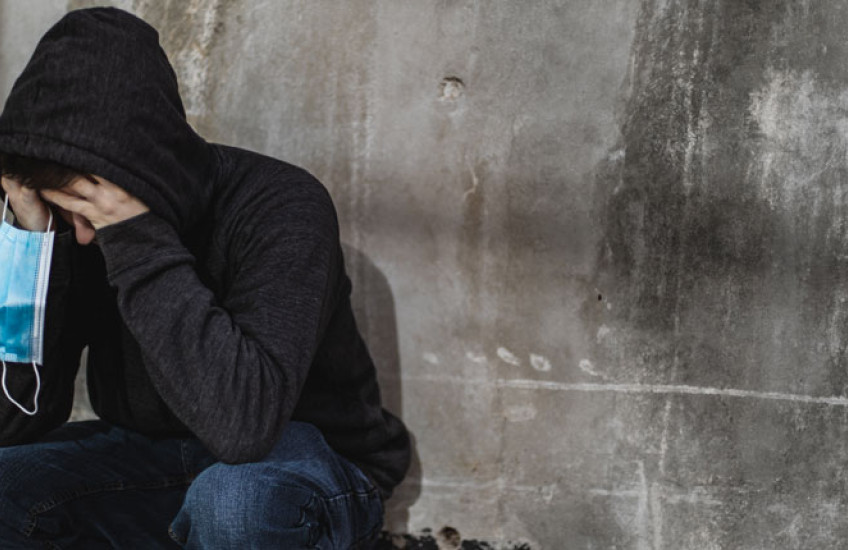 Person with a hoodie on holding their face in their hands, and also holding a mask