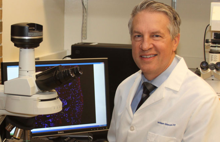William Giannobile in a white lab coat at computer and microscope