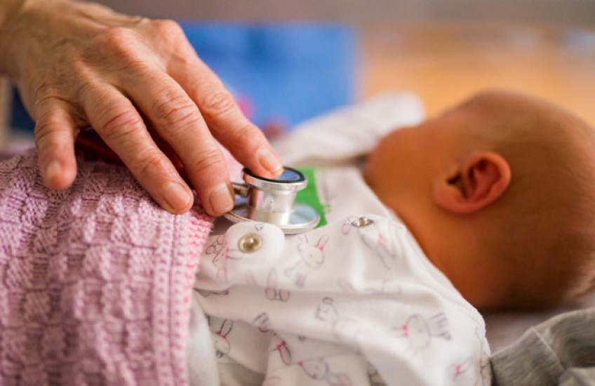 Photo of a hand with a stethoscope on a newborn baby's chest 