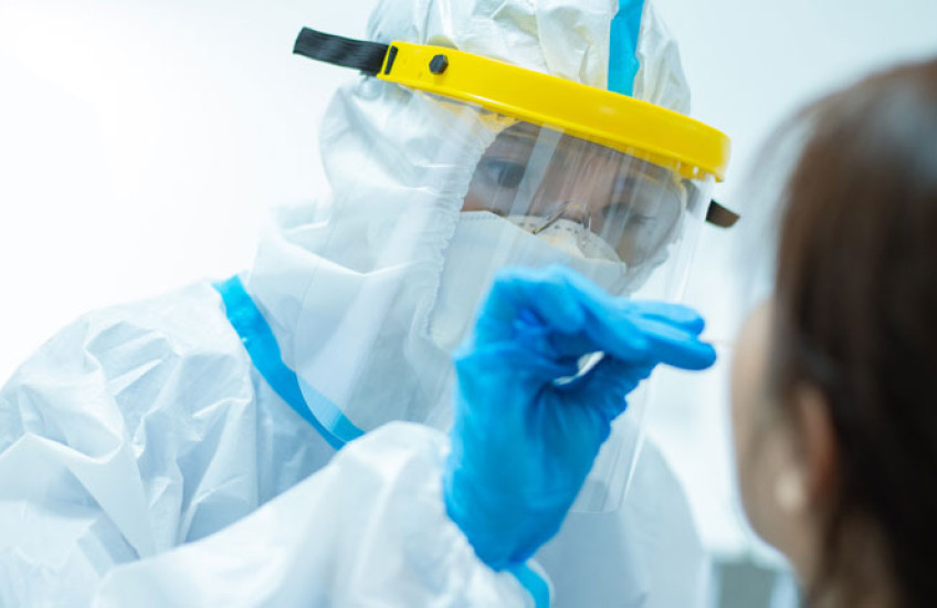 Person in full PPE obtaining a nasal swab specimen from a patient 