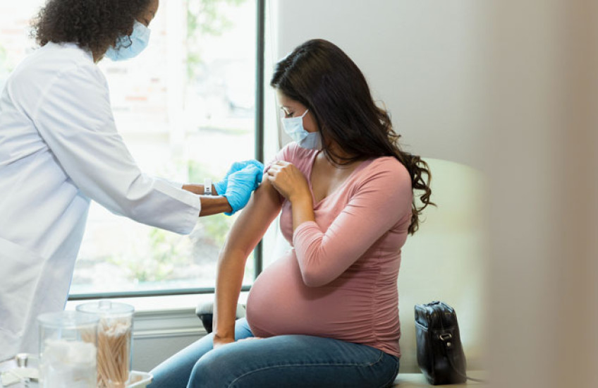 A doctor prepares a pregnant person's arm for a vaccine