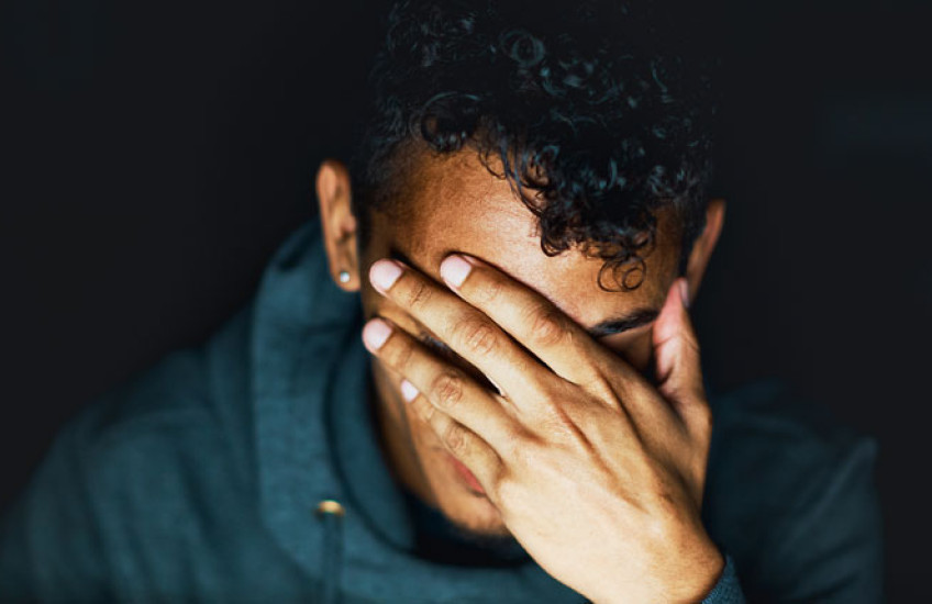 A close up of a person with their hand covering their face against a black background