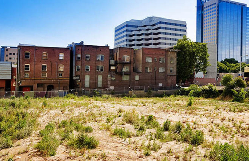 Urban setting showing older low-rise brick housing wedged between an empty dirt lot and modern glass-sided high-rise buildings