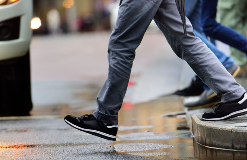 The lower half of a person stepping off a curb to cross the street in front of a car