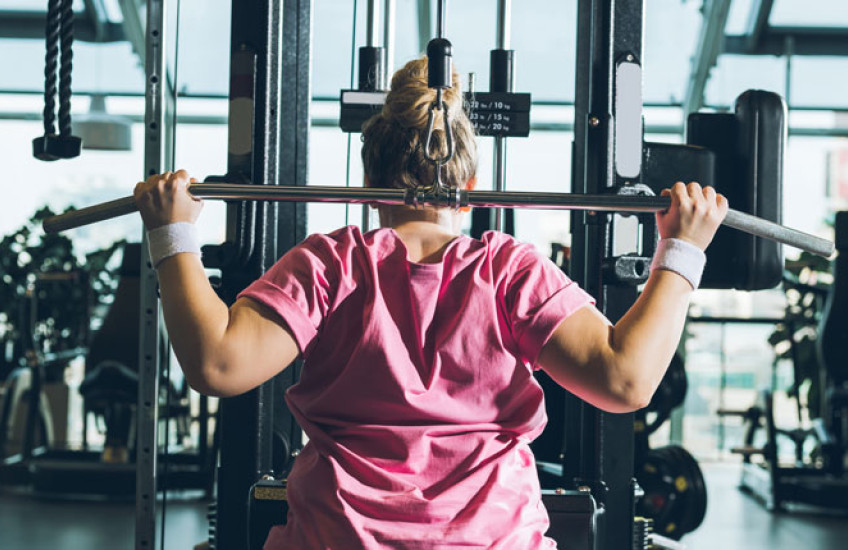 Photo of woman in pink top lifting weights in a gym