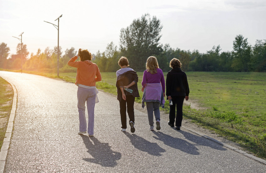 Four adult women walking side-by-side on a path surrounded by green grass