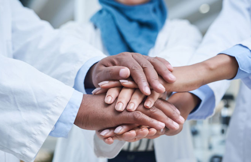 Close up of the stacked hands of three physicians with different ethnicities in solidarity.