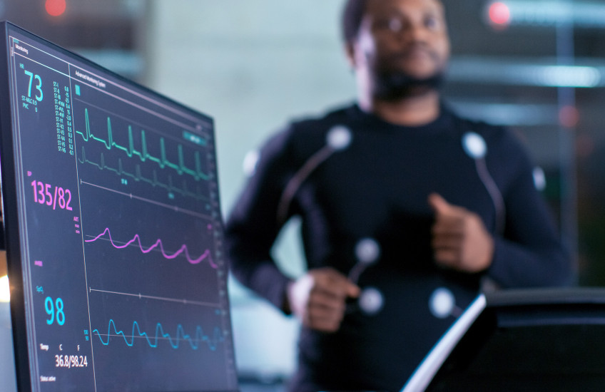 Blurred image of a man on a treadmill with electrodes attached and connected to a heart monitor in a research lab