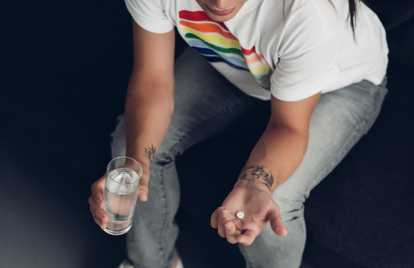 young transgender man with pill and glass of water sitting on couch 