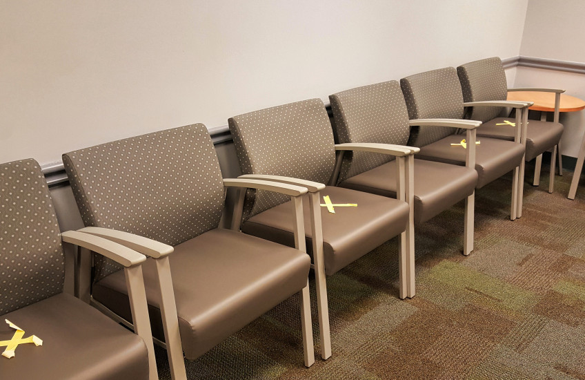 Empty chairs in waiting room, marked with X's for social distancing