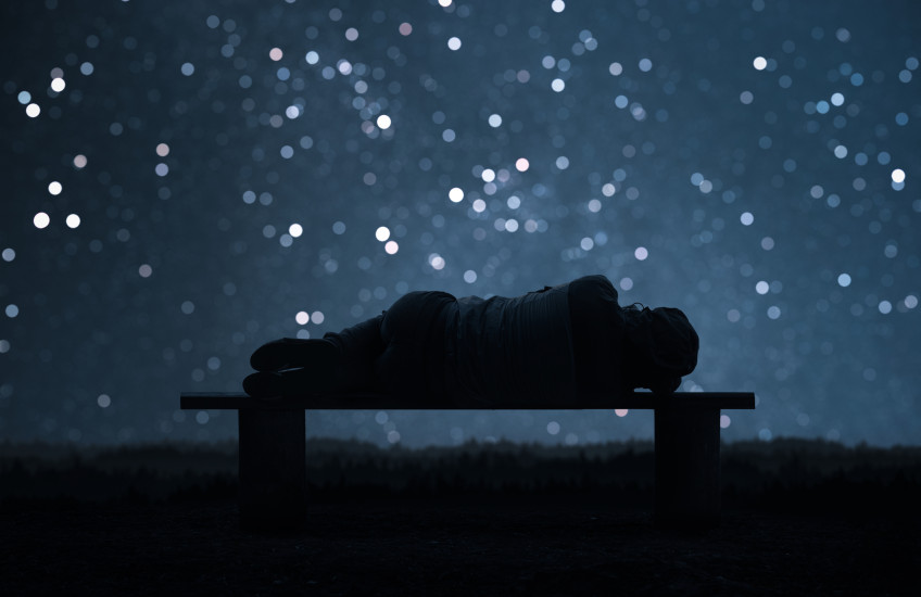 Photo illustration of a sleeping female form in silhouette with a backdrop of a night sky and stars