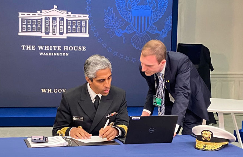Murthy in uniform seated at table looking at laptop with Beckman to right leaning in; a backdrop behind them reads The White House