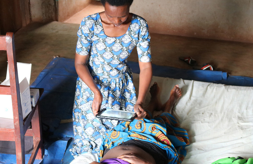 A female health care worker uses a tablet computer to take a photo of a woman lying on a bed