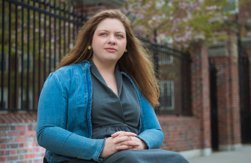 Cloutier sitting in wheel chair with arms folded in lap wearing a green button down and aqua sweater
