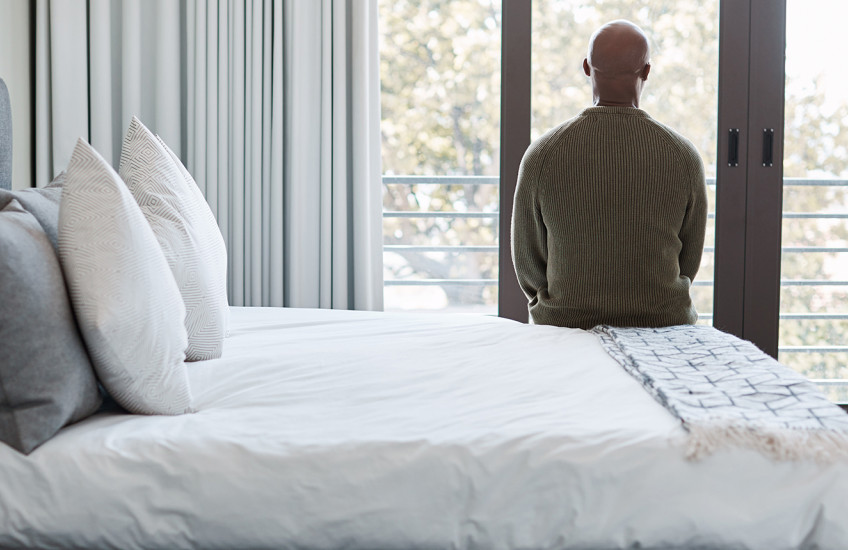 Rearview shot of a mature man looking through a window in a bedroom.