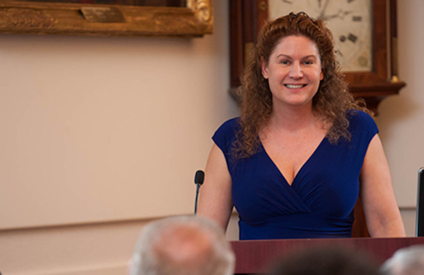 Woman in a dress stands at a podium in front of audience members