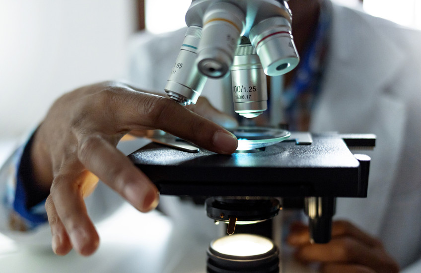 Closeup on the hands of a man in a white lab coat looking in microscope in a medical laboratory.