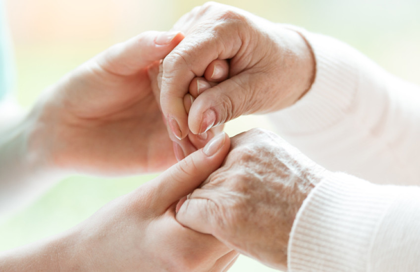 Image: a caregiver holding hands with a hospice patient
