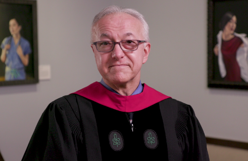 Dean Daley, wearing academic regalia, speaking in Gordon Hall